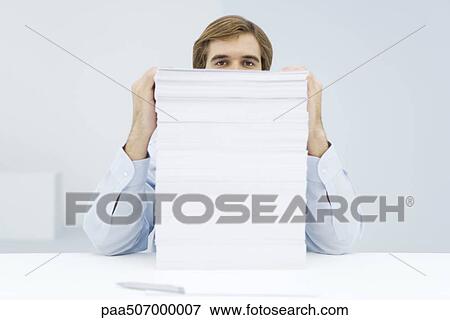 Stock Photo - Man peering over tall stack of paper. Fotosearch