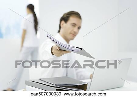 Stock Photo - Professional man handing folder to camera, focus on foreground. Fotosearch