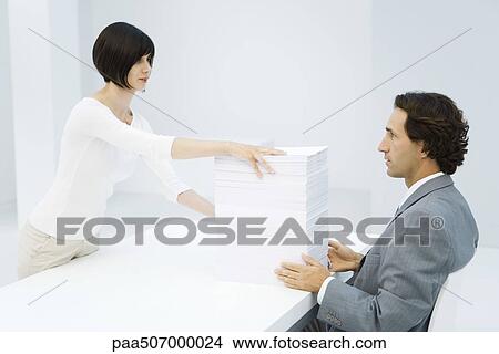 Professional woman and businessman exchanging tall stack of paper across desk View Large Photo Image Picture - Professional woman and businessman exchanging tall stack of paper across desk. Fotosearch