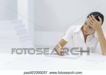 Woman holding her forehead, writing on blank sheet of paper, looking at staggered pile of paper View Large Photo Image Stock Photo - Woman holding her forehead, writing on blank sheet of paper, looking at staggered pile of paper. Fotosearch