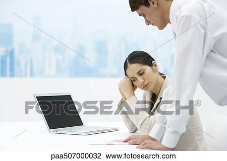 Woman looking down and holding head, colleague leaning on desk and looking over her shoulder View Large Photo Image Stock Image - Woman looking down and holding head, colleague leaning on desk and looking over her shoulder. Fotosearch