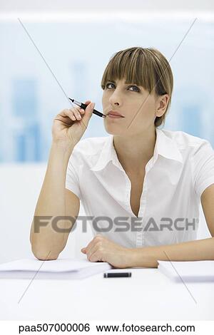 Stock Photograph - Woman looking up and holding pen up to her cheek. Fotosearch