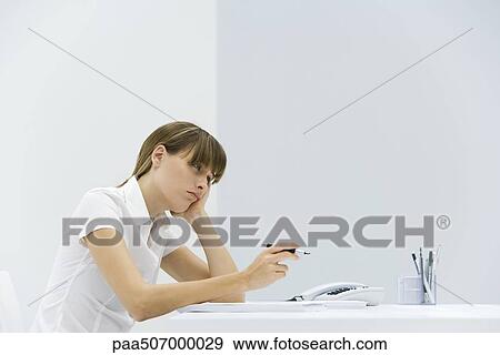 Woman sitting at desk, resting head in her hand, looking away and frowning View Large Photo Image Stock Photo - Woman sitting at desk, resting head in her hand, looking away and frowning. Fotosearch
