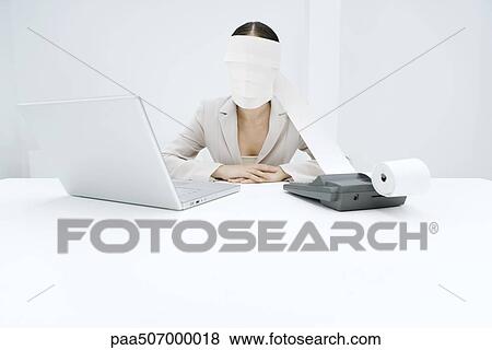 Woman sitting at desk with adding machine and laptop, printout tape wrapped around head View Large Photo Image Stock Photo - Woman sitting at desk with adding machine and laptop, printout tape wrapped around head. Fotosearch
