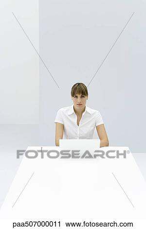 Woman sitting at table with laptop, looking at camera View Large Photo Image Stock Image - Woman sitting at table with laptop, looking at camera. Fotosearch
