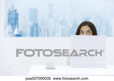 Stock Photography - Woman sitting behind stack of paper, looking over and away. Fotosearch