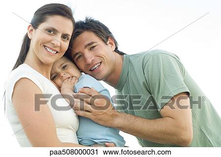Family smiling at camera, mother holding baby daughter, father leaning in and gently hugging the baby View Large Photo Image Stock Image - Family smiling at camera, mother holding baby daughter, father leaning in and gently hugging the baby. Fotosearch