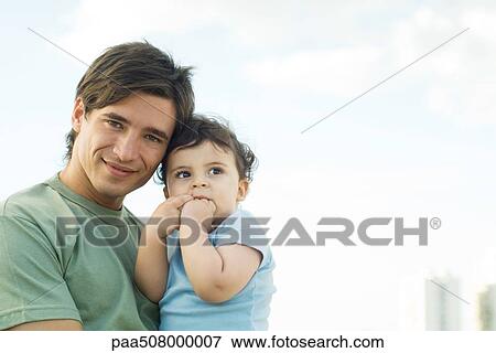 Stock Photo - Father holding baby, smiling at camera. Fotosearch