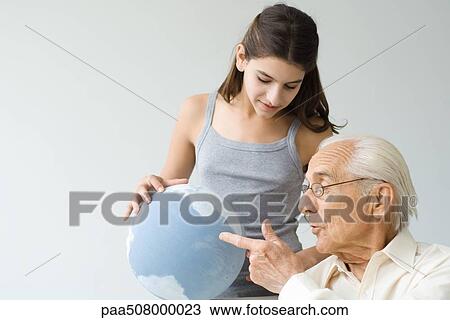Stock Image - Grandfather and granddaughter looking at globe together. Fotosearch