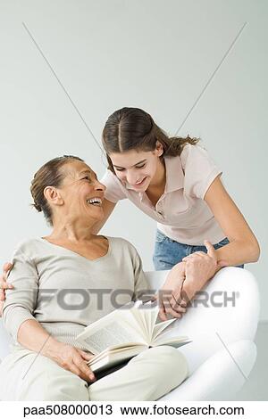 Stock Image - Grandmother holding book, granddaughter looking over her shoulder. Fotosearch