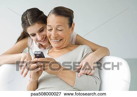 Grandmother holding cell phone, granddaughter looking over her shoulder View Large Photo Image Stock Photo - Grandmother holding cell phone, granddaughter looking over her shoulder. Fotosearch