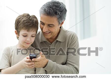 Mature man and young son looking at cell phone together View Large Photo Image Stock Image - Mature man and young son looking at cell phone together. Fotosearch