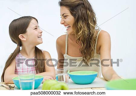Mother and daughter sitting at table, laughing at each other View Large Photo Image Stock Image - Mother and daughter sitting at table, laughing at each other. Fotosearch