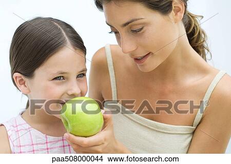 Picture - Mother giving daughter an apple, both smiling. Fotosearch