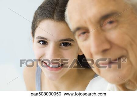 Stock Image - Teen girl looking over grandfather's shoulder, both smiling, focus on background. Fotosearch