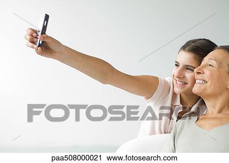Teenage girl photographing self and grandmother with cell phone, both smiling View Large Photo Image Stock Image - Teenage girl photographing self and grandmother with cell phone, both smiling. Fotosearch