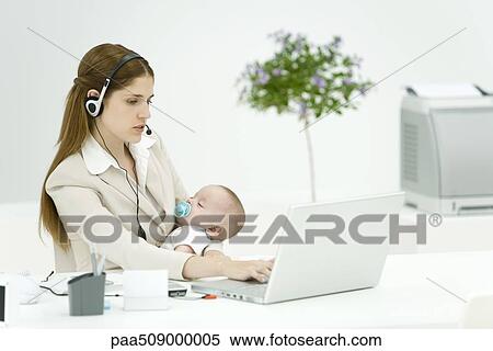 Businesswoman in office, holding sleeping baby, using headset and laptop computer View Large Photo Image Stock Photography - Businesswoman in office, holding sleeping baby, using headset and laptop computer. Fotosearch