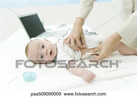 Stock Photo - Mother changing baby's diaper on desk, laptop computer in background, cropped view. Fotosearch