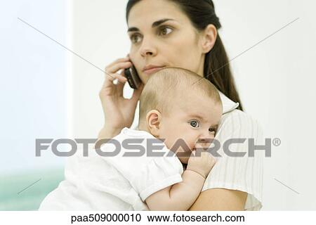 Mother holding infant, using cell phone View Large Photo Image Stock Image - Mother holding infant, using cell phone. Fotosearch