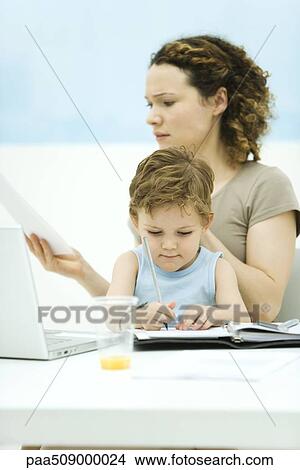 Mother holding son on lap, sitting in front of laptop, frowning at document View Large Photo Image Picture - Mother holding son on lap, sitting in front of laptop, frowning at document. Fotosearch
