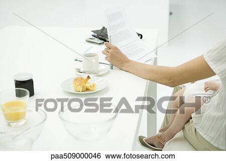 Mother sitting at breakfast table, reading document, infant sleeping on lap, cropped view View Large Photo Image Stock Photograph - Mother sitting at breakfast table, reading document, infant sleeping on lap, cropped view. Fotosearch