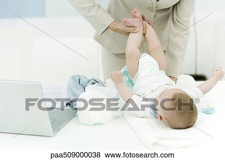 Stock Photo - Professional woman changing baby's diaper on desk, cropped view. Fotosearch