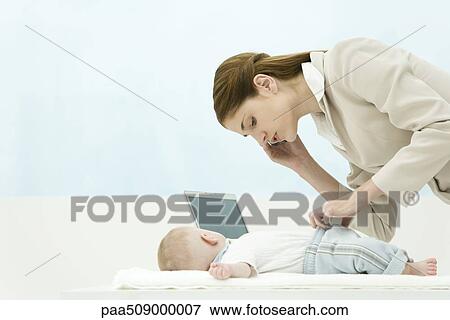 Stock Photo - Professional woman in office, using cell phone, bending over baby on desk. Fotosearch
