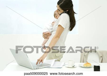 Professional woman standing beside breakfast table, holding baby, using cell phone and laptop computer View Large Photo Image Stock Photography - Professional woman standing beside breakfast table, holding baby, using cell phone and laptop computer. Fotosearch