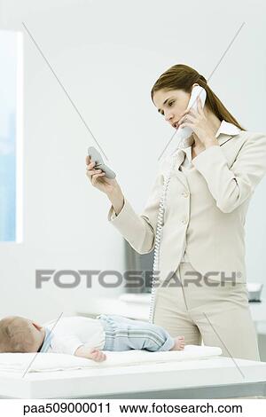 Professional woman talking on phone, looking at self in mirror compact, baby lying on desk nearby View Large Photo Image Stock Image - Professional woman talking on phone, looking at self in mirror compact, baby lying on desk nearby. Fotosearch