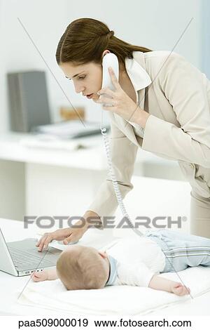 Professional woman using phone and laptop computer, baby lying on desk beside her View Large Photo Image Stock Photo - Professional woman using phone and laptop computer, baby lying on desk beside her. Fotosearch