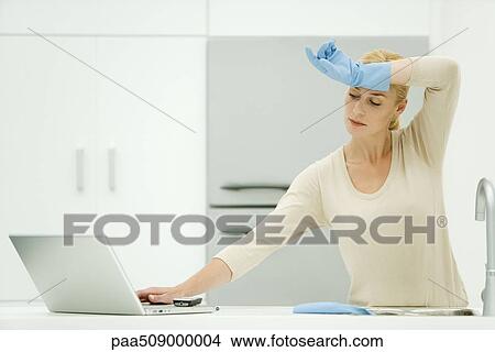 Woman standing at kitchen sink, reaching for laptop computer, wearing rubber gloves View Large Photo Image Picture - Woman standing at kitchen sink, reaching for laptop computer, wearing rubber gloves. Fotosearch