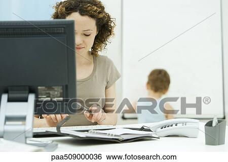 Woman working at computer in home office, young son playing in background View Large Photo Image Stock Photograph - Woman working at computer in home office, young son playing in background. Fotosearch