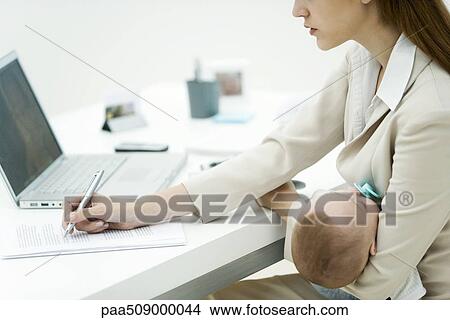 Young professional woman in office, holding sleeping infant, signing document View Large Photo Image Picture - Young professional woman in office, holding sleeping infant, signing document. Fotosearch