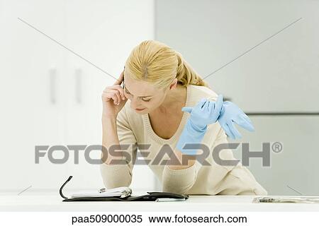 Young woman wearing rubber gloves, using cell phone and looking down at agenda View Large Photo Image Stock Photography - Young woman wearing rubber gloves, using cell phone and looking down at agenda. Fotosearch
