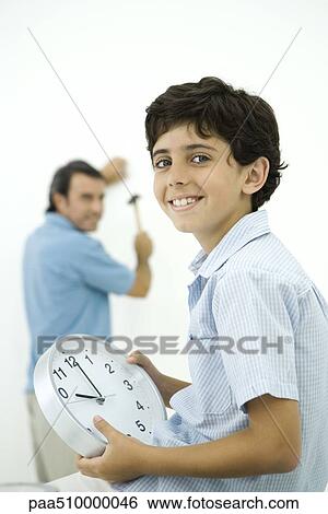 Boy holding clock and smiling at camera, father holding hammer in background View Large Photo Image Stock Photograph - Boy holding clock and smiling at camera, father holding hammer in background. Fotosearch