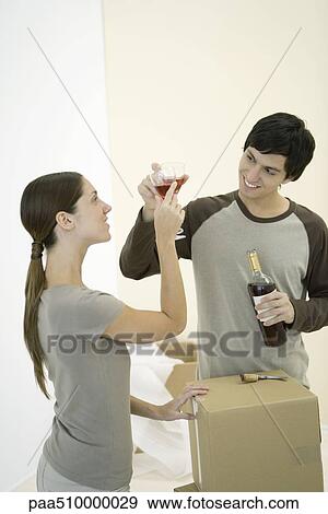Stock Photo - Couple clinking glasses of red wine, cardboard boxes nearby. Fotosearch