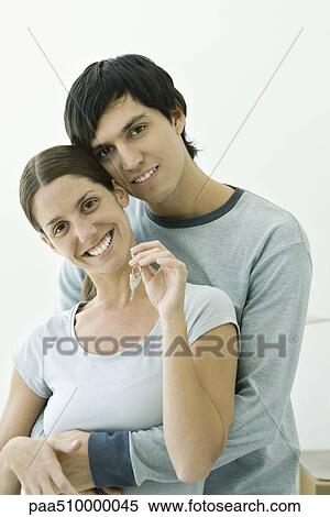 Stock Photography - Couple embracing and smiling at camera, woman holding up key. Fotosearch