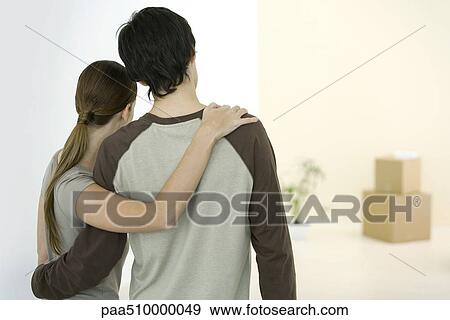 Stock Photo - Couple embracing, looking at new home, rear view. Fotosearch