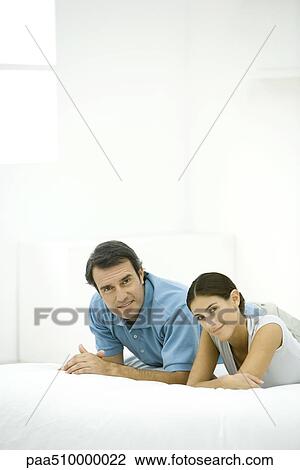 Stock Image - Couple lying on bed, smiling at camera. Fotosearch