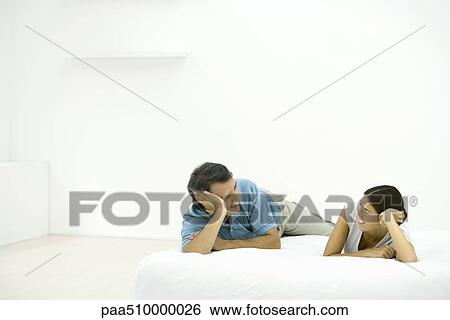 Stock Photograph - Couple lying on bed, smiling at each other. Fotosearch