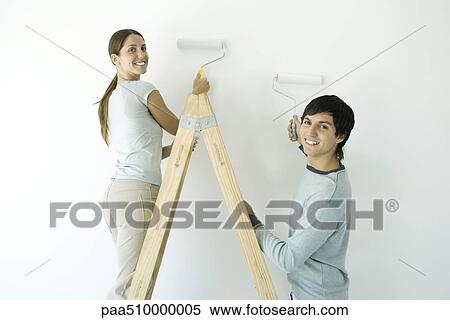 Stock Photography - Couple painting wall with rollers, both smiling over their shoulder at camera. Fotosearch