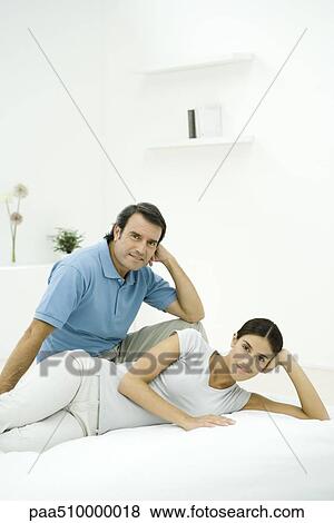 Stock Photo - Couple relaxing together on bed, both smiling at camera. Fotosearch