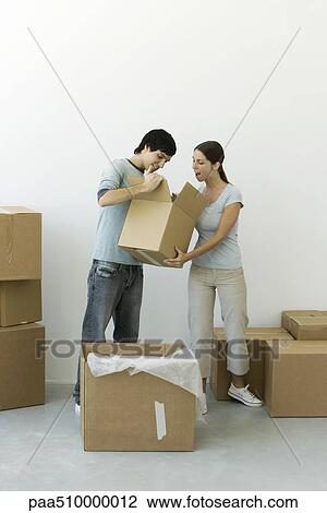 Stock Image - Couple unpacking, man showing contents of one box, woman's mouth open in surprise. Fotosearch