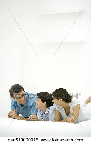 Family lying on bed together, smiling at each other View Large Photo Image Stock Photograph - Family lying on bed together, smiling at each other. Fotosearch