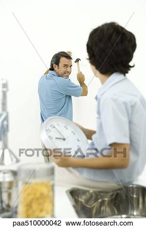 Stock Image - Man holding hammer, smiling over shoulder at son holding clock in foreground. Fotosearch