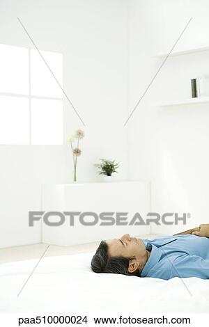 Man lying on back on bed, eyes closed View Large Photo Image Picture - Man lying on back on bed, eyes closed. Fotosearch
