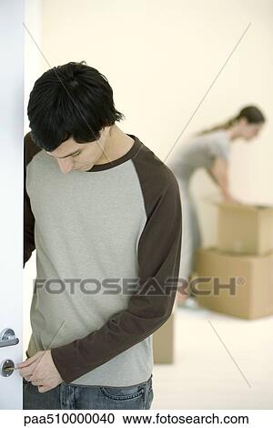 Stock Image - Man testing key on door lock, woman unpacking boxes in background. Fotosearch