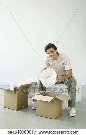 Man unpacking boxes, holding lampshade, smiling at camera View Large Photo Image Stock Photo - Man unpacking boxes, holding lampshade, smiling at camera. Fotosearch