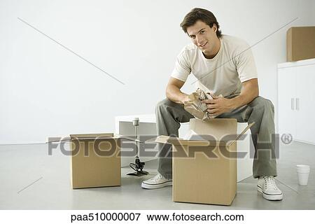 Stock Photo - Man unpacking boxes, sitting on bench, smiling at camera. Fotosearch