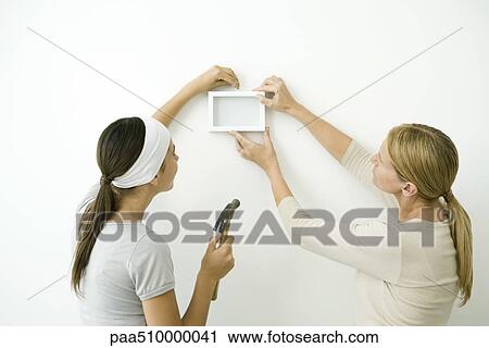 Stock Image - Mother and daughter attaching picture frame to wall. Fotosearch